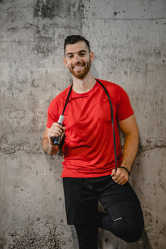 Portrait of happy male fitness instructor with skipping rope isolated on gray background