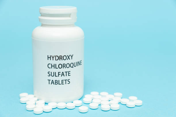 istock Treatments for Coronavirus (COVID-19): HYDROXYCHLOROQUINE in white bottle packaging with scattered pills. Isolated on blue background. Horizontal shot. Copy space 1256869373