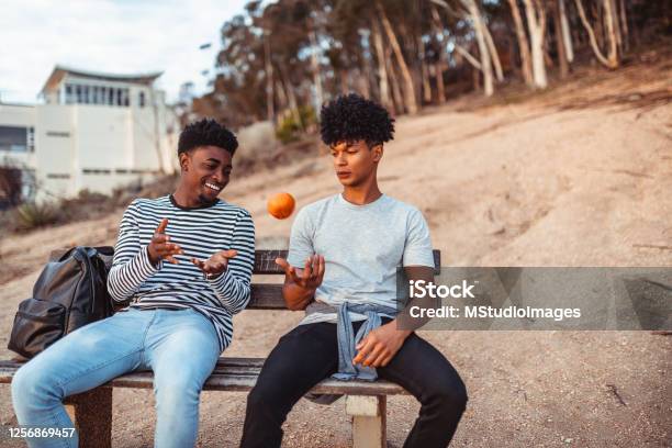 Young man juggling with the orange and talking to his friend