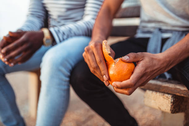 Man pealing orange while sitting with a friend on the bench Man pealing orange while sitting with a friend on the bench peeling food stock pictures, royalty-free photos & images