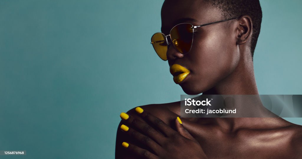 Female model bright makeup and sunglasses Close-up shot of female model bright makeup and sunglasses on grey background. Attractive african woman with buzzcut posing in studio. Melanin Stock Photo