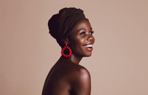 Smiling african woman with a turban Close up of smiling african woman on beige background. Beautiful female model with a cloth wrapped on head looking away and smiling. melanin photos stock pictures, royalty-free photos & images
