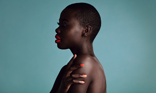 Profile view of stylish woman with metalic red lipstick and nailpaint. African female model with buzzcut on grey background.