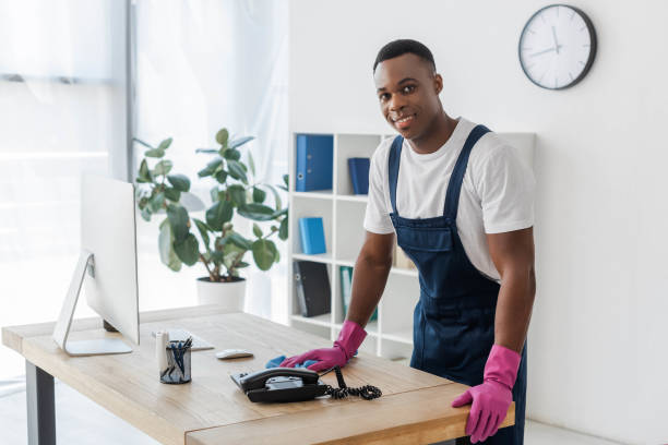 istock Smiling african american cleaner with rag standing near office table 1256885567