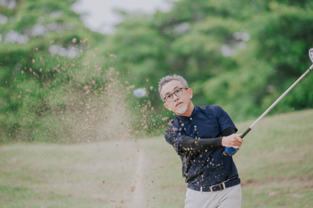 ein asiatischer chinesischer senior-mann golfer schlägt seinen golfball in einer sandfalle mit seinem eisenschläger - golf power golf course challenge stock-fotos und bilder