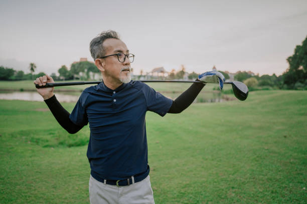 un asiático chino senior hombre golfista llevando su palo de golf en su hombro y mirando la vista en el campo de golf - retirement golfer happiness relaxation fotografías e imágenes de stock
