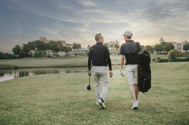 un asiático chino senior hombre golfista caminando y hablando con su hijo que lleva una bolsa de golf al final del juego felizmente en el campo de golf de melaka - retirement golfer happiness relaxation fotografías e imágenes de stock