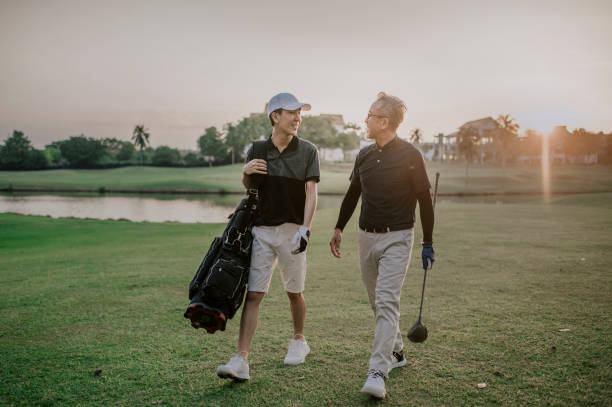 un asiático chino senior hombre golfista caminando y hablando con su hijo que lleva una bolsa de golf al final del juego felizmente en el campo de golf de melaka - retirement golfer happiness relaxation fotografías e imágenes de stock