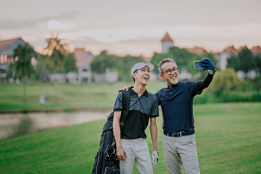 an asian chinese senior man golfer having selfie with his son after winning the golf game with toothy smile