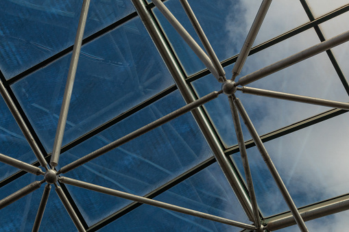Elaborate steel metal greenhouse structure with diffuse view of deep blue sky with clouds, horizontal aspect