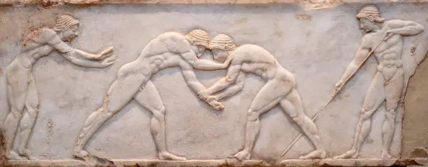 Ancient bas-relief on ancient Greek funerary stele from Kerameikos in Athens, Greece. Scene from Palaestra - wrestlers in action. On the left an athlete is ready to jump, on the right another one prepairing the pit.
