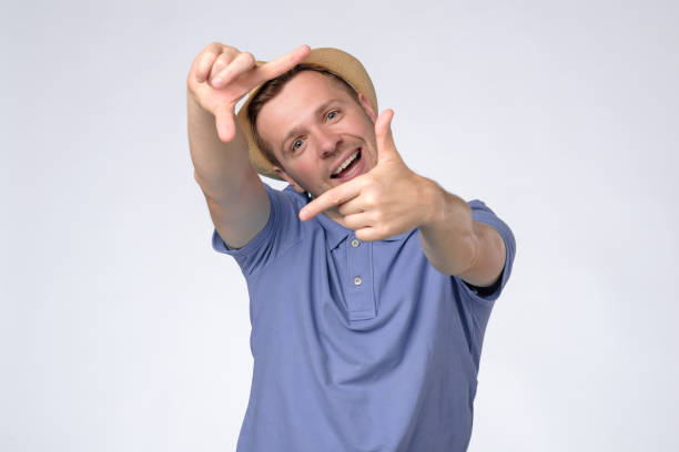 istock Curious man in summer hat gesturing picture frame with hands, looking through fingers 1256900690