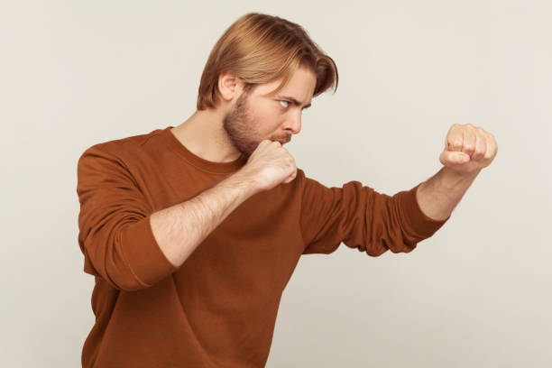 je vais te frapper ! vue latérale de l’homme dans le sweat-shirt restant avec le geste levé de boxe de poings, menaçant de poinçonner - men sweat combative sport boxing photos et images de collection