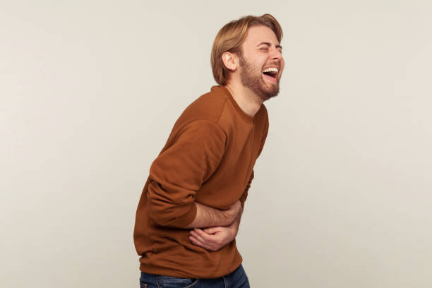Hilarious laughter. Portrait of amused man with beard wearing sweatshirt holding belly and laughing out loud Hilarious laughter. Portrait of amused man with beard wearing sweatshirt holding belly and laughing out loud after hearing crazy anecdote, funny joke. indoor studio shot isolated on gray background hysteria stock pictures, royalty-free photos & images