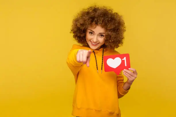 Photo of Internet blogging. Portrait of cheerful curly-haired woman in urban style hoodie pointing to camera