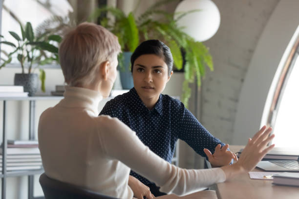 Indian and caucasian businesswomen negotiating sit at desk in office Indian and caucasian businesswomen negotiating sit at desk in office. Lawyer consulting client during formal meeting. Job interview and hiring process. Diverse colleagues discussing project concept serious business stock pictures, royalty-free photos & images