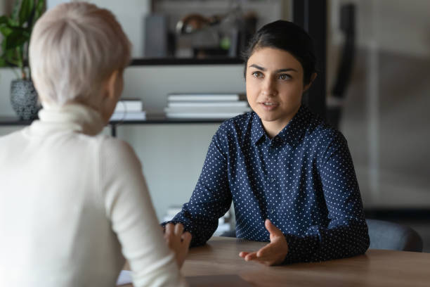 Indian applicant and caucasian HR manager communication during job interview Multi ethnic indian and caucasian diverse young businesswomen sitting in front of each other in office during business meeting. HR manager and vacancy candidate talk, job interview and hiring concept serious stock pictures, royalty-free photos & images