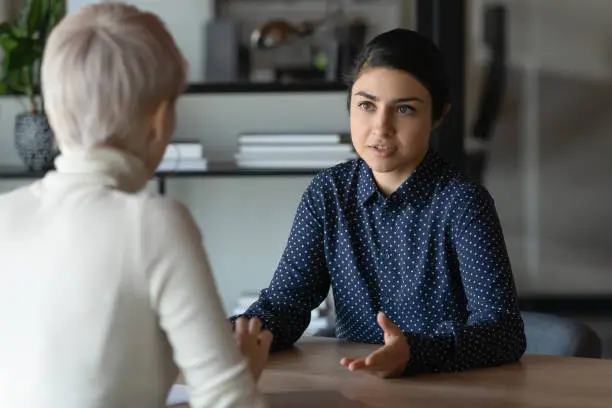 Multi ethnic indian and caucasian diverse young businesswomen sitting in front of each other in office during business meeting. HR manager and vacancy candidate talk, job interview and hiring concept