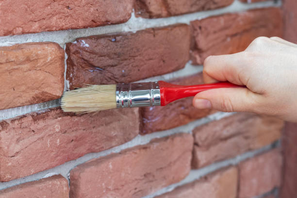 istock Process of varnishing grout between gypsum decorative bricks. Covering brick wall with waterproofing coating. 1256908359