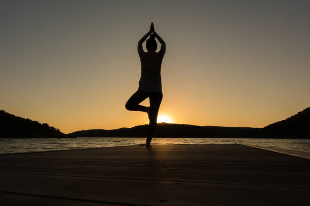 istock young girl doing yoga poses on a pier at sunset. Tree pose 1256908545
