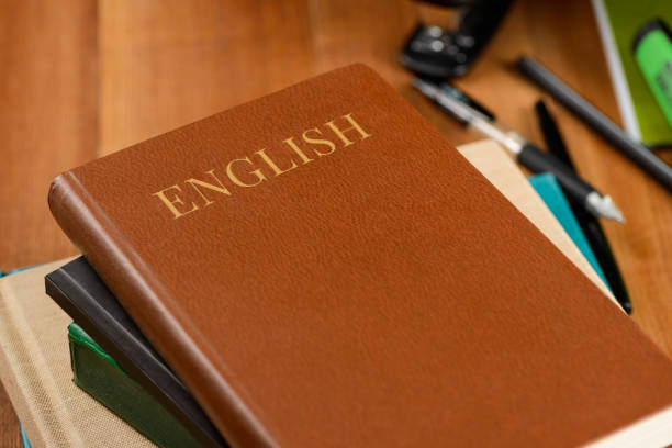 Books and office products on wooden desktop. English school book, brown leather. Education concept.