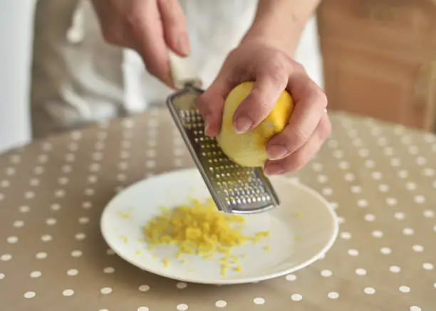 Closeup of woman rubbing lemon zest on grater