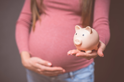 Pregnant woman with piggy bank, saving money to her newborn baby. Money saving, donation, economizing, pregnancy, finance, investment, fund and life insurance concept.