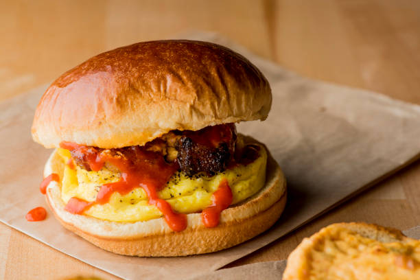 petit déjeuner sandwich au bacon, œufs et fromage. petit déjeuner classique ou brunch préféré. bacon fumé croustillant à l’érable servi avec des œufs sur du hachage de pommes de terre de campagne facile et épicé avec des oignons et des poivro - biscuit sausage sandwich breakfast photos et images de collection