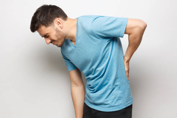 junge unglückliche kerl in blauen t-shirt leiden unter schweren rückenschmerzen, berühren den rücken versuchen, schmerzen in der wirbelsäule zu lindern, isoliert auf grauem hintergrund - backache massaging pain back stock-fotos und bilder