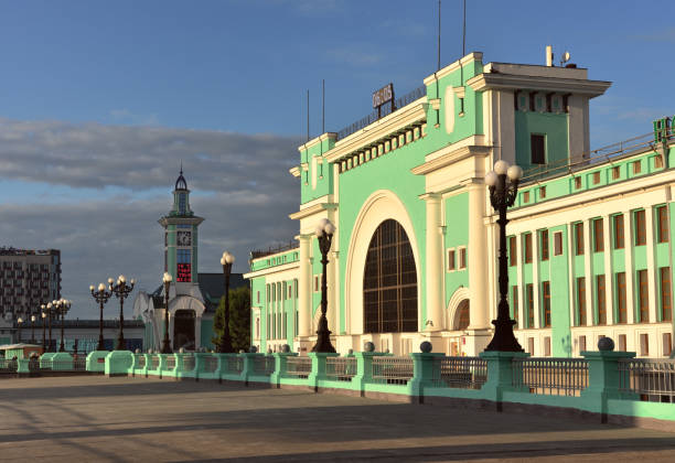 Novosibirsk-Main train station in the morning The facade of the largest railway station in Siberia in the style of constructivism in the morning contrasting light, a deserted square, a large arched window, blue sky, clouds, a tower in the distance. Space for text. Novosibirsk, Russia, 2020 western siberia stock pictures, royalty-free photos & images