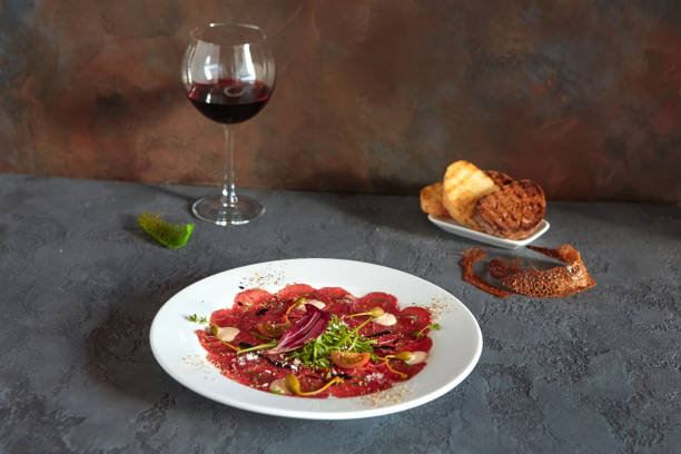 carpaccio de viande dans une plaque blanche sur un fond en bois, avec le pain et le vin délicieux dans un verre - carpaccio red meat caper bread photos et images de collection