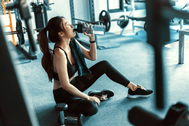 istock woman taking a break and  drinking water after workout at gym. 1256962904