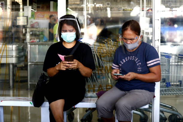 Ladies with face shield and mask use their phone while outside a store during the Covid 19 outbreak stock photo