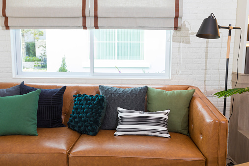 Leather sofa with green pillows and blanket in elegant living room interior with modern coffee table.