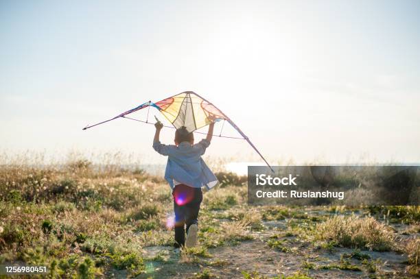 Brave New World Concept Of Little Active Sport Boy Running With Kite Above His Head Towards Sunset Sea Horizon Stock Photo - Download Image Now