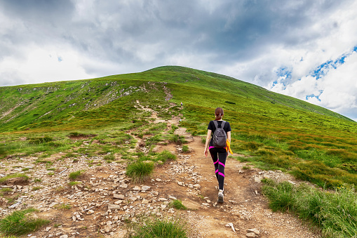 A young girl with a backpack climbs a mountain. Beautifull cloudy sky. Leisure. Hiking. Hoverla Mountain. Ukraine. Healthy lifestyle.