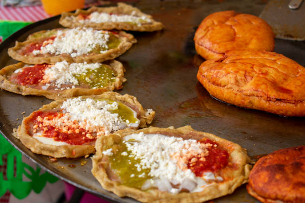 mexikanische küche: zubereitung von "sopes, gekniffen, gehackt oder gehackt"" mit käse und heißer soße, und auch "pambazos" in einem "comal". "comal" ist ein traditioneller küchencontainer, der als bügeleisen verwendet wird. es ist ein straßenessen. - arbol stock-fotos und bilder