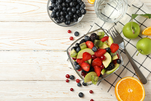 Composition with cup of fresh fruit salad on white wooden table, top view