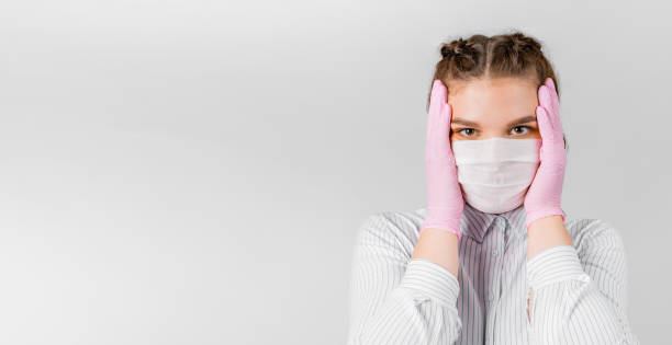 joven mujer con camisa blanca, en una máscara médica y guantes estériles rosas está sosteniendo la cabeza en las manos sobre un fondo blanco. se sorprendió. el concepto de autoaislado, protección, cuarentena - middle eastern ethnicity teenage girls women sadness fotografías e imágenes de stock