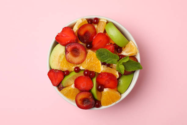 istock Bowl of fresh fruit salad on pink background, top view 1256989037