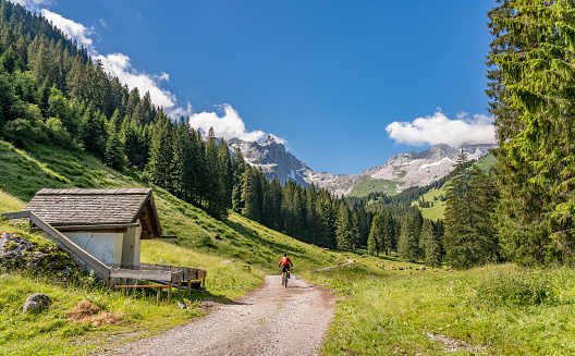 senior woman riding her electric mountain bike up to the Lindau Hut below the famous summits of Drusenfluh and Three towers in the Montafon Area of Vorarlberg Austria