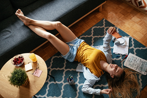 Favorite Pastime. Cheerful Young Black Woman Lying On Couch And Listening Music In Wireless Headphones, Happy African American Female Having Fun At Home, Resting In Living Room, Free Space