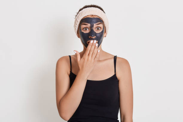 Emotional surprised Caucasian woman looks with shocked expression directly at camera, stands against white background, cleans her skin with mud cosmetic mask. Emotional surprised Caucasian woman looks with shocked expression directly at camera, stands against white background, cleans her skin with mud cosmetic mask. sooth stock pictures, royalty-free photos & images