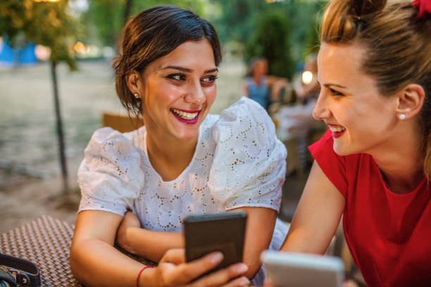istock Two girls are sitting at a cafe and having fun using mobile phones 1256999723