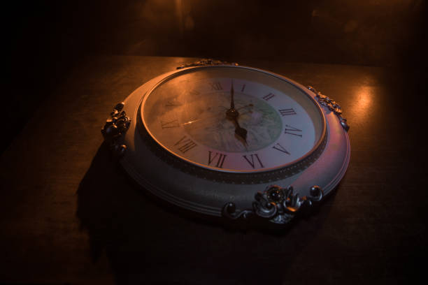 Time concept. Big vintage round clock on wooden table with abstract light. Dark atmosphere. Creative decoration. Selective focus