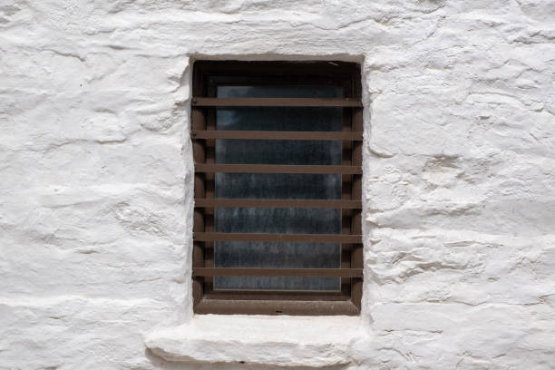 Brown color painted window with security bars on a white stone wall, greek island architecture, copy space. Holidays in Greece card template