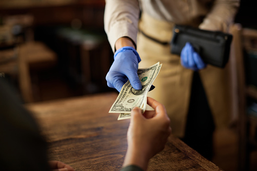Close-up of waitress wearing protective gloves while taking money from a customer in a pub.