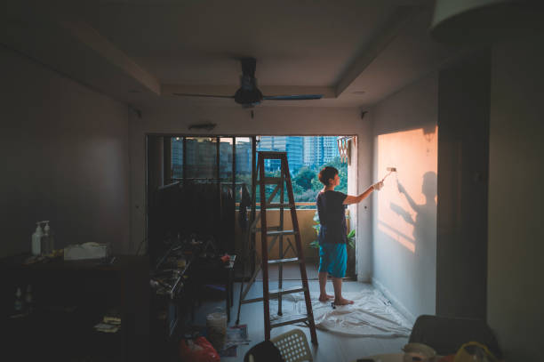 una femmina asiatica cinese di mezza adulta che dipinge il suo soggiorno, ristrutturazione dell'appartamento durante il tramonto - shadow focus on shadow women sunset foto e immagini stock