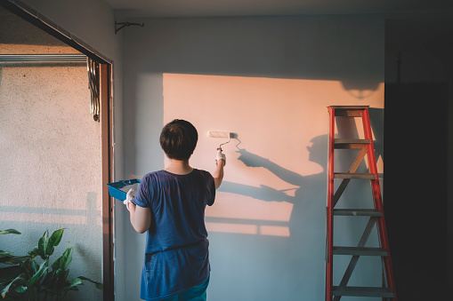 una asiática china media adulta hembra pintura de su sala de estar, renovación de apartamentos durante la puesta del sol photo