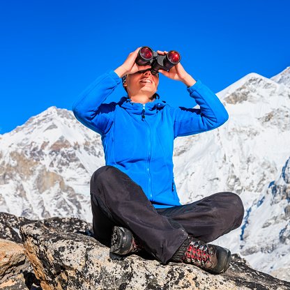 Woman looking through binoculars at Mount Everest in Sagarmatha National Park. Mount Everest - also called Qomolangma Peak, Mount Sagarmatha, Chajamlungma (Limbu), Zhumulangma Peak or Mount Chomolungma - is the highest mountain on Earth, and the highest point on the Earth's continental crust, as measured by the height above sea level of its summit, 8,848 metres (29,029 ft). The mountain, which is part of the Himalaya range in Asia, is located on the border between Sagarmatha Zone, Nepal, and Tibet, China.